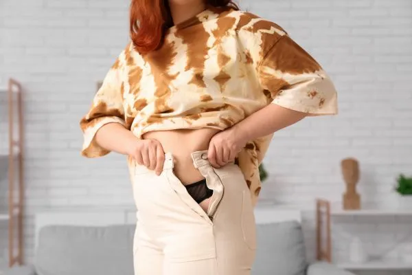Image of woman trying to do her trousers up after pregnancy weight gain Runnymede